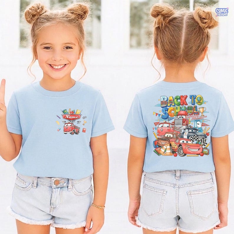 May include: A light blue short-sleeve t-shirt featuring a small graphic of a red fire truck and school supplies on the front chest, and a large colorful graphic on the back with the text BACK TO SCHOOL and various cartoon race cars.