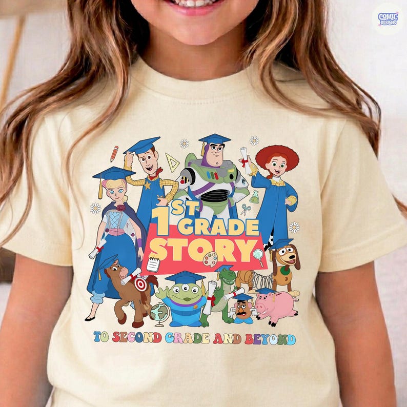 May include: A light yellow t-shirt featuring a colorful graphic of animated characters in graduation caps. The text "1st Grade Story" is prominently displayed, with the phrase "To Second Grade and Beyond" below. The design includes various cartoon figures.