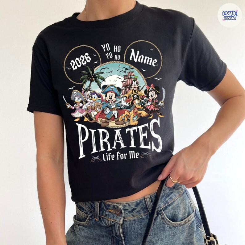 May include: Black t-shirt featuring a pirate-themed design with cartoon characters. The design includes the text "2026", "Yo Ho Yo Ho", and "Pirates life for me". The shirt has a crew neck and short sleeves.