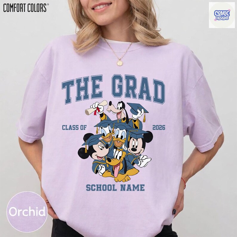 Puede incluir: Camiseta color orqu&iacute;dea con el texto "THE GRAD" en azul, con personajes de Disney con atuendo de graduaci&oacute;n. La camiseta incluye el texto "CLASS OF 2026" y "SCHOOL NAME". La camiseta es de Comfort Colors.
