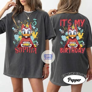 Puede incluir: Camiseta gris oscuro con un pato de dibujos animados sosteniendo un pastel de cumplea&ntilde;os. La parte delantera de la camiseta dice "Sophia" y "3". La parte trasera de la camiseta dice "It's My Birthday". La camiseta tiene un aspecto vintage.