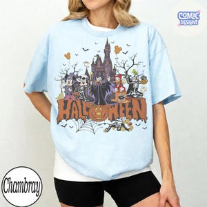Puede incluir: Una camiseta azul claro con un estampado gr&aacute;fico de personajes de dibujos animados con disfraces de Halloween frente a un castillo. El dise&ntilde;o incluye el texto HALLOWEEN en letras grandes de color naranja, murci&eacute;lagos, una telara&ntilde;a y una calabaza.