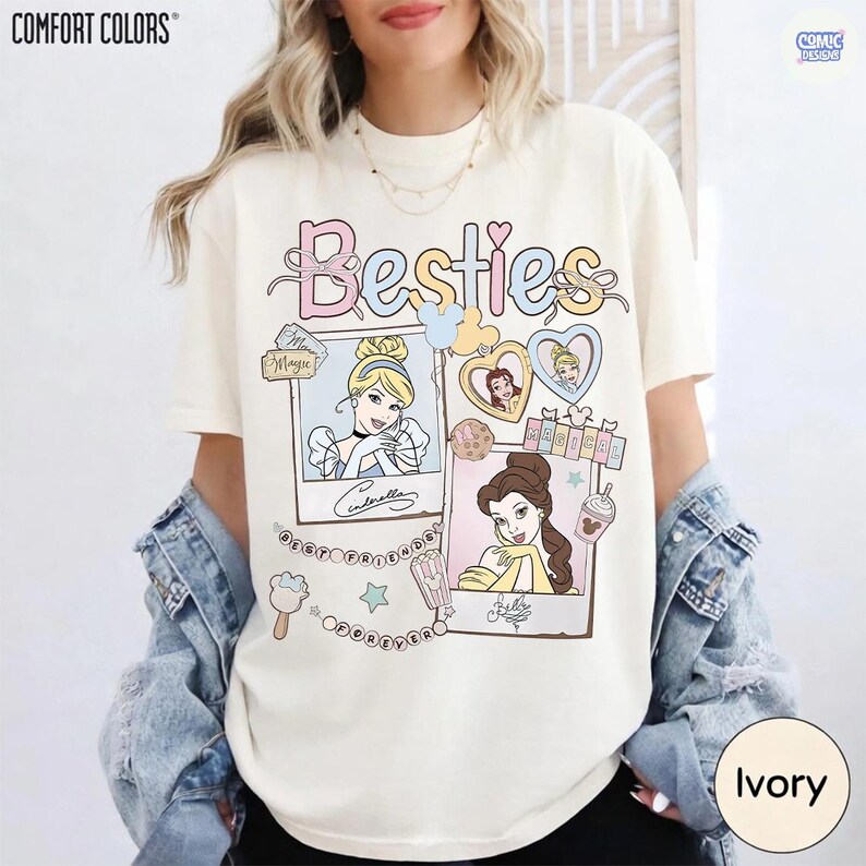 Puede incluir: Camiseta de color marfil con la palabra "Besties" en colores pastel. La camiseta presenta ilustraciones de princesas de Disney en marcos estilo polaroid. El logo de Comfort Colors est&aacute; en la parte superior izquierda.