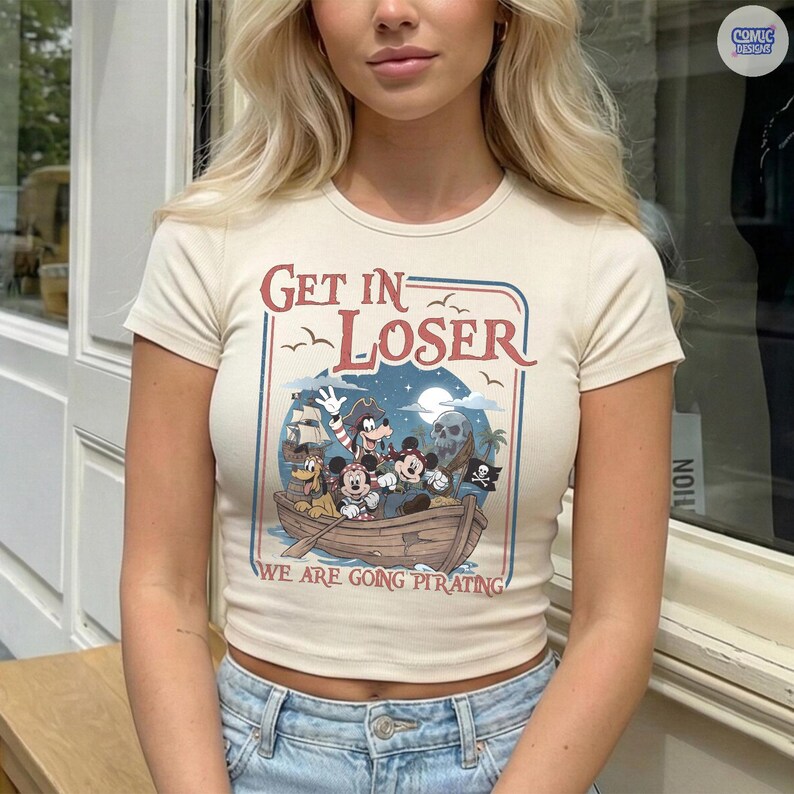 May include: Cream-colored, short-sleeved crop top with the text "GET IN LOSER" above a cartoon pirate scene. The graphic features Disney characters in a boat, with the phrase "WE ARE GOING PIRATING" below.