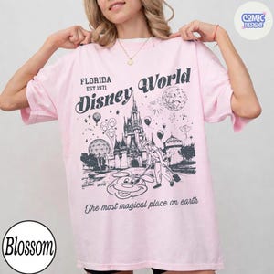 K&ouml;nnte beinhalten: Hellrosa T-Shirt mit einer Grafik des Florida Disney World Schlosses, Mickey Mouse und dem Text "The most magical place on earth". Das Shirt hat auch den Text "Florida Est. 1971" und "Disney World".