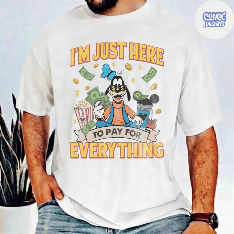 May include: White t-shirt featuring a cartoon character holding money, popcorn, and a drink. The shirt has the text "I'M JUST HERE TO PAY FOR EVERYTHING" in orange and yellow.