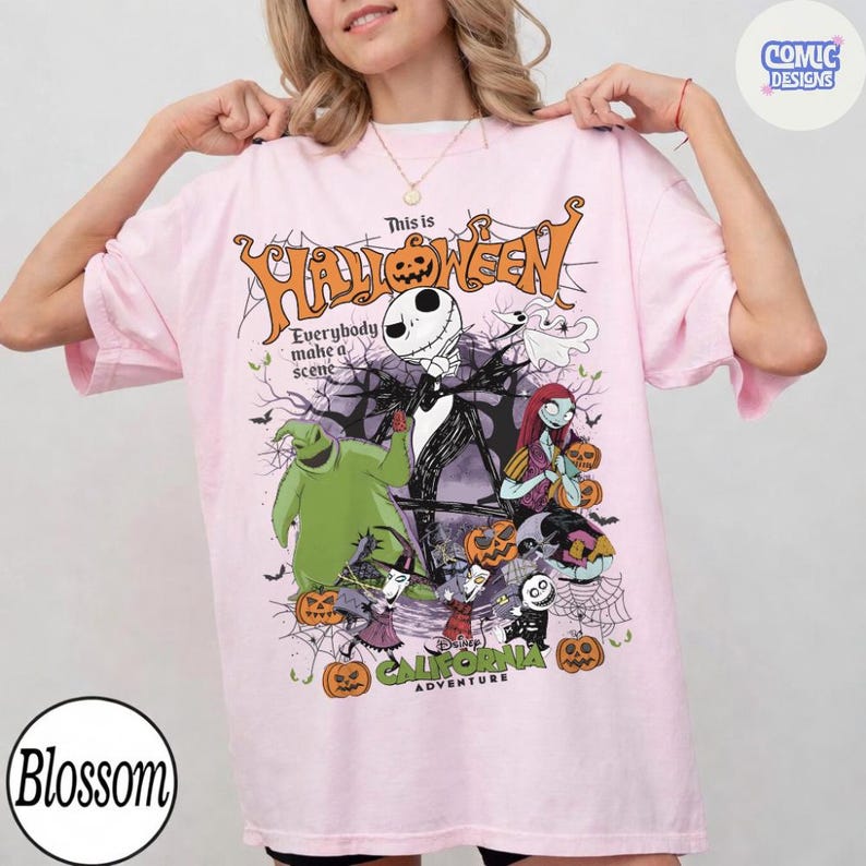 May include: Light pink t-shirt featuring a Halloween-themed graphic. The design includes Jack Skellington, Sally, and other characters from "The Nightmare Before Christmas." The text "This is Halloween" and "California Adventure" are also visible.