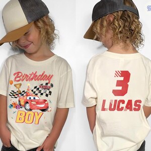 Puede incluir: Camiseta color crema con un coche de carreras rojo y el texto "Birthday BOY". La parte trasera de la camiseta muestra un gran n&uacute;mero rojo "3" y el nombre "LUCAS". La camiseta est&aacute; dise&ntilde;ada para una fiesta de cumplea&ntilde;os.