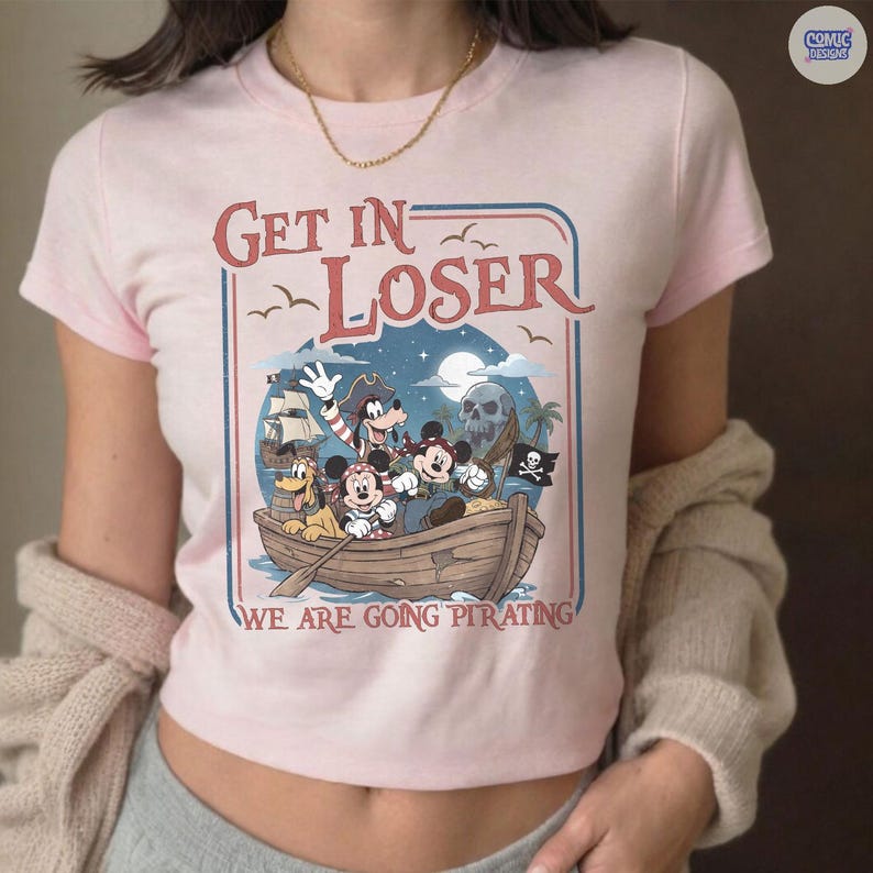 May include: Pink t-shirt with a pirate-themed graphic. The design features a boat with cartoon characters, a skull, and the text "Get In Loser, We Are Going Pirating."