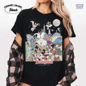 Puede incluir: Camiseta negra con un gr&aacute;fico colorido de personajes y atracciones de Disneyland. El dise&ntilde;o incluye a Dumbo, Peter Pan, Mickey y Minnie Mouse, y el texto "Disneyland California, 1955". La camiseta tiene las palabras "Comfort Colors Black" impresas.