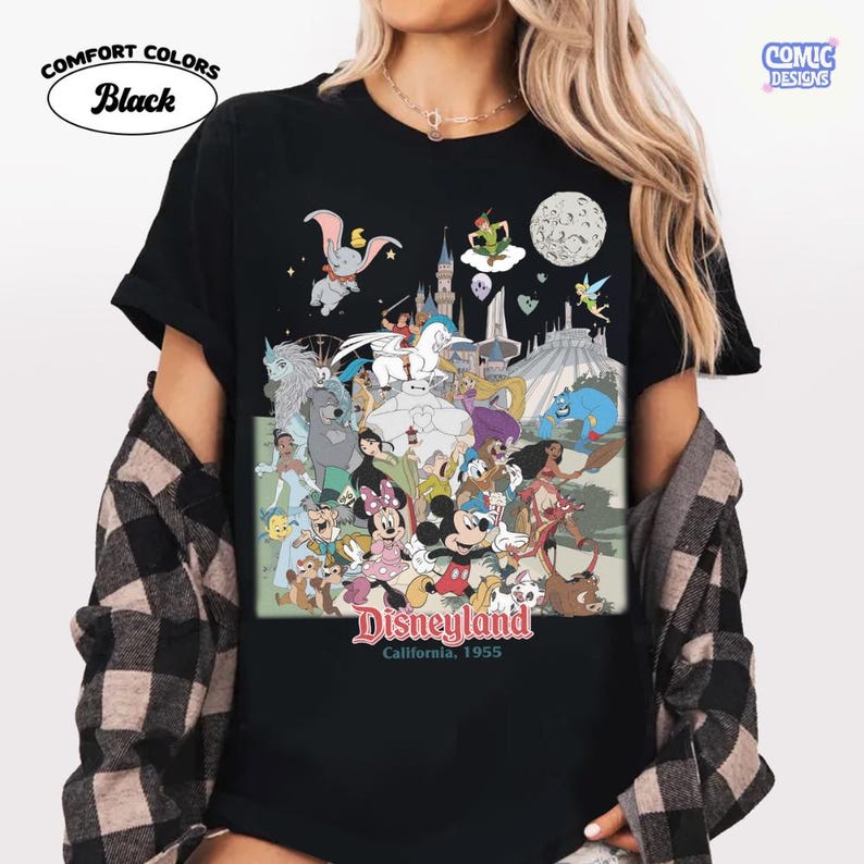 Puede incluir: Camiseta negra con un gr&aacute;fico colorido de personajes y atracciones de Disneyland. El dise&ntilde;o incluye a Dumbo, Peter Pan, Mickey y Minnie Mouse, y el texto "Disneyland California, 1955". La camiseta tiene las palabras "Comfort Colors Black" impresas.