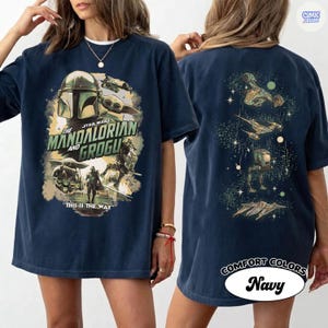 Op de afbeelding: Marineblauwe t-shirt met een afbeelding uit de serie The Mandalorian. De voorkant toont de Mandalorian en Grogu, met de tekst "The Mandalorian and Grogu" en "This is the Way". De achterkant toont ruimteschepen.