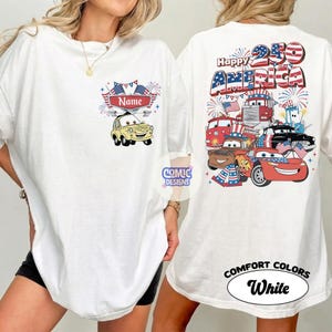 May include: White t-shirt with a patriotic design. The front features a yellow cartoon car and the word "Name" above it. The back displays "Happy 250 America" with cartoon cars, flags, and fireworks. The shirt is labeled "Comfort Colors White".