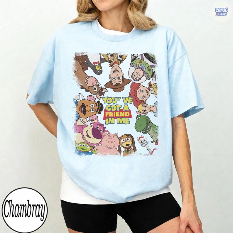 May include: Light blue t-shirt featuring a colorful graphic of characters from the animated film "Toy Story." The graphic includes the text "You've Got a Friend in Me." The shirt is a casual, short-sleeved style.