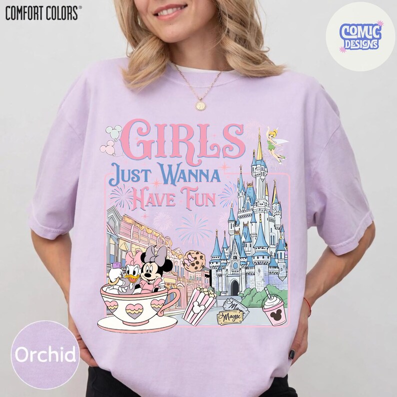 May include: Orchid-colored t-shirt with the text "GIRLS JUST WANNA HAVE FUN" and a graphic featuring Disney characters, a castle, and other theme park elements. The shirt is from Comfort Colors and has a Comic Designs logo.