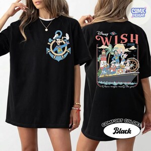 May include: Black t-shirt featuring Mickey Mouse as a captain inside a blue anchor on the front. The back of the shirt has a Disney Wish 2026 graphic with Mickey, Donald, and other characters on a ship. The shirt is labeled "Comfort Colors Black."