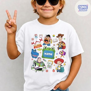 May include: A white short-sleeved t-shirt featuring a colorful graphic print of various Toy Story characters including Woody, Buzz Lightyear, Jessie, Mr. Potato Head, and Forky, along with a green frame containing the text 1st GRADE STORY and Name.