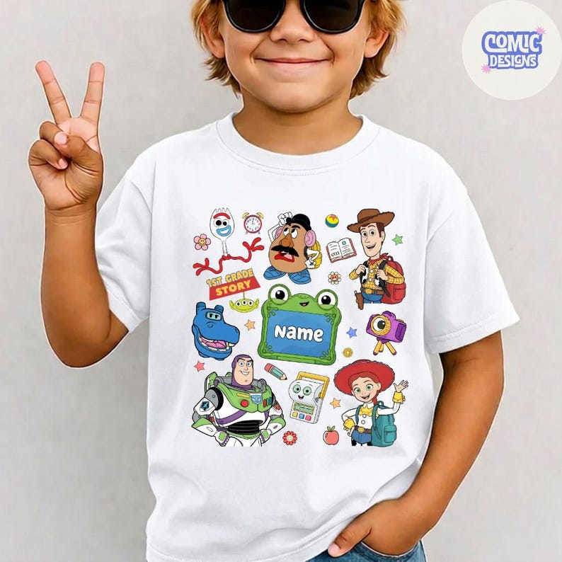 May include: A white short-sleeved t-shirt featuring a colorful graphic print of various Toy Story characters including Woody, Buzz Lightyear, Jessie, Mr. Potato Head, and Forky, along with a green frame containing the text 1st GRADE STORY and Name.