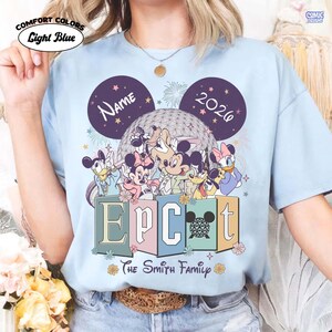 May include: Light blue Comfort Colors t-shirt featuring a Disney-themed design. The design includes Disney characters, the word "EPCOT", the year "2026", and the text "The Smith Family". The shirt also has the word "Name" on it.