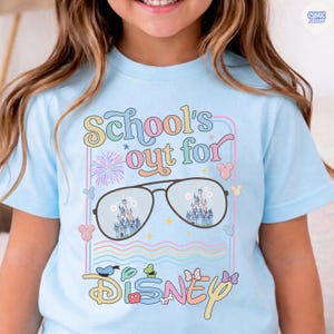 Może przedstawiać: Jasnoniebieska koszulka z napisem "School's out for Disney" w kolorowej, zabawnej czcionce. Projekt zawiera okulary przeciwsłoneczne odbijające zamek, fajerwerki i ikony Myszki Miki. Zabawny, fantazyjny design dla fana Disneya.