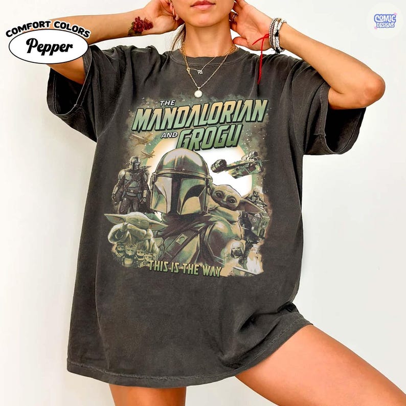 May include: Dark gray Comfort Colors t-shirt featuring a graphic from The Mandalorian and Grogu. The design includes the Mandalorian, Grogu, and text that reads "This is the Way". The shirt also has the text "COMIC DESIGNS" and "Pepper" on it.