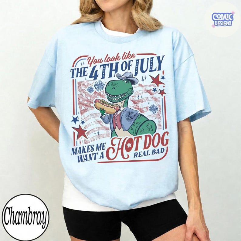 May include: Light blue t-shirt with a graphic featuring a dinosaur holding a hot dog, an American flag, and the text "You look like the 4th of July. Makes me want a hot dog real bad."