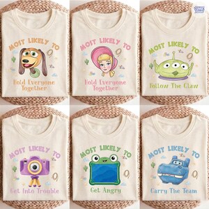 May include: Six cream-colored t-shirts featuring cartoon graphics and text. Designs include a dog with 'Most Likely To Hold Everyone Together', a character with a pink hat, an alien with 'Most Likely To Follow The Claw', a camera, a frog, and a hippo.