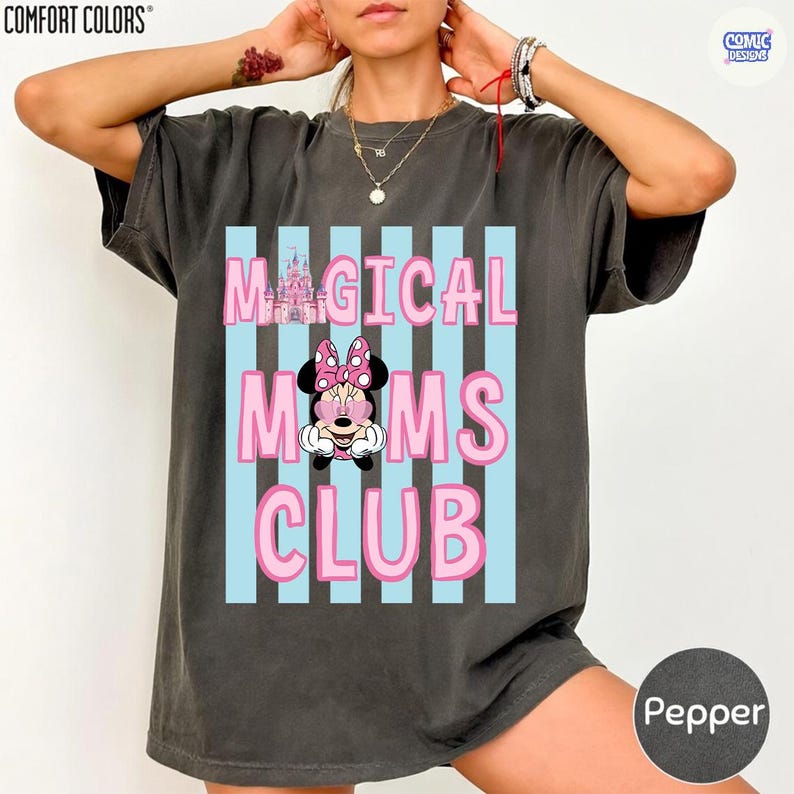 K&ouml;nnte beinhalten: Dunkelgraues T-Shirt mit dem Text "MAGICAL MOMS CLUB" in Rosa, vor hellblauen vertikalen Streifen. Eine Cartoon-Grafik von Minnie Mouse ist unter dem Text zentriert. Das Shirt ist von der Marke Comfort Colors.