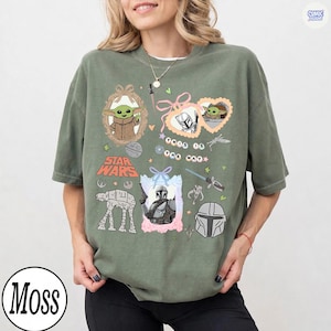 Puede incluir: Camiseta verde oliva con gr&aacute;ficos de Star Wars. El dise&ntilde;o incluye im&aacute;genes de Grogu, el Mandaloriano y un caminante AT-AT. Tambi&eacute;n est&aacute; presente el texto "This is the Way". La camiseta tiene un corte holgado.