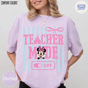 May include: Orchid-colored t-shirt with the words "TEACHER MODE OFF" in pink, featuring a Minnie Mouse graphic. The design includes light blue vertical stripes and a pink bow. The shirt is from Comfort Colors.