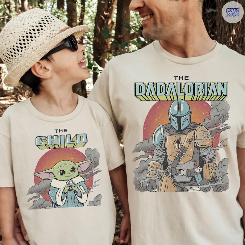 Puede incluir: Camisetas beige con gr&aacute;ficos a juego. Una camiseta presenta "THE CHILD" con un dibujo animado de Grogu, la otra dice "THE DADALORIAN" con una ilustraci&oacute;n de Mandaloriano. Ambos dise&ntilde;os incluyen un sol rojo y humo.