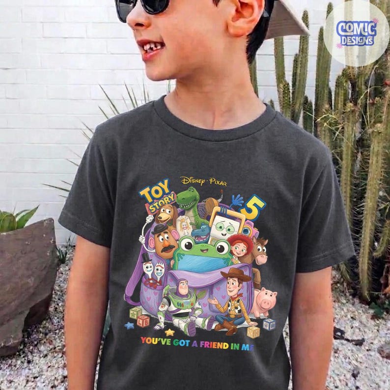 May include: A charcoal grey t-shirt featuring a colourful graphic of Toy Story characters emerging from a purple backpack. The design includes Buzz Lightyear, Woody, Rex, Mr. Potato Head, and others, with the text Toy Story 5 and You've Got A Friend In Me.