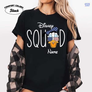 May include: Black Comfort Colors t-shirt with a Disney Squad design. The design features Donald Duck wearing sunglasses with a patriotic stars and stripes pattern. The word "Name" is below the Donald Duck graphic.