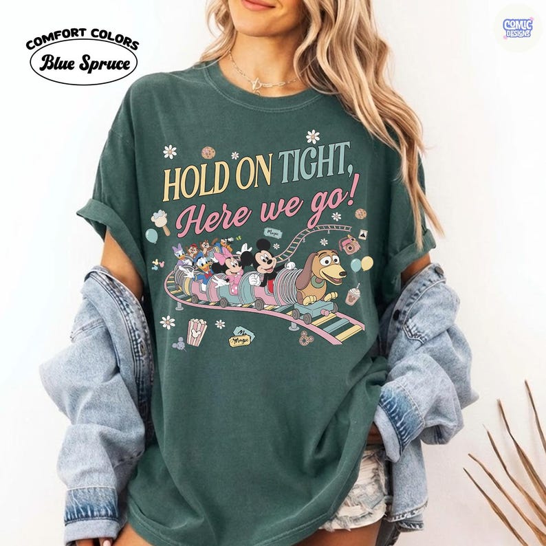 May include: Dark green t-shirt with the text "HOLD ON TIGHT, Here we go!" and a cartoon roller coaster design featuring Mickey Mouse, Donald Duck, and other characters. The shirt is labeled "Comfort Colors Blue Spruce".