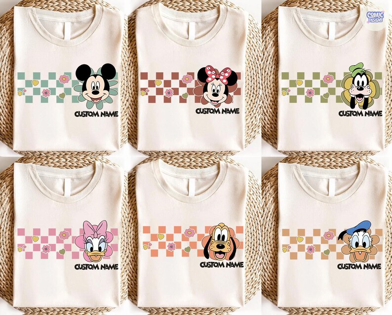 May include: Six cream-colored t-shirts featuring cartoon characters Mickey Mouse, Minnie Mouse, Goofy, Daisy Duck, Pluto, and Donald Duck. Each shirt has a checkered pattern with flowers and the text "CUSTOM NAME" below the character.