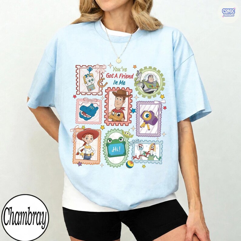 May include: A light blue t-shirt featuring a graphic print of various Toy Story characters arranged in postage stamp-style frames. The text "You've Got A Friend In Me" is printed in the center, surrounded by illustrations of Woody, Buzz Lightyear, Jessie, and other characters.