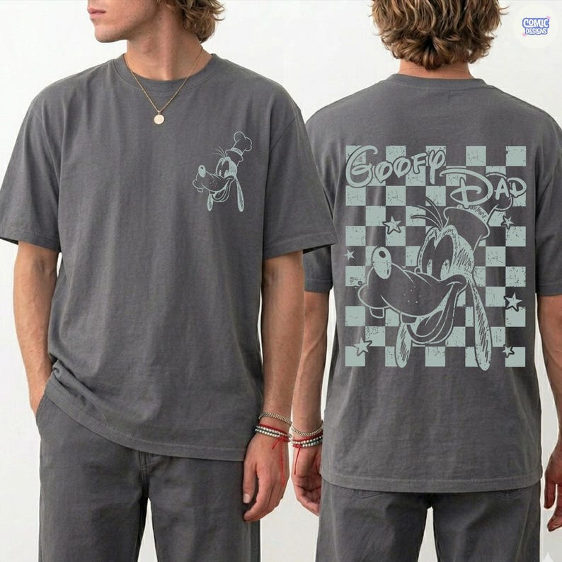 May include: Gray t-shirt featuring a light blue graphic of Goofy wearing a chef's hat on the front. The back of the shirt displays Goofy with the text "Goofy Dad" on a checkered background. The shirt is short-sleeved.