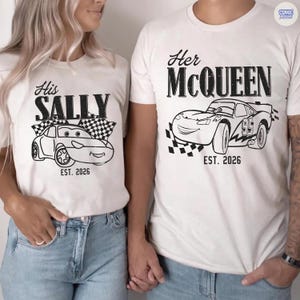 May include: Matching white t-shirts with black graphics. One shirt says "His SALLY" with a cartoon car and checkered flag, the other says "Her McQUEEN" with a cartoon car and checkered flag. Both shirts have "EST. 2026".