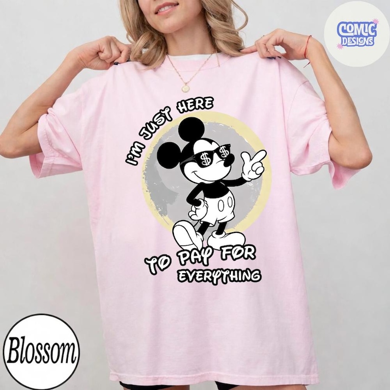May include: Light pink t-shirt featuring a black and white Mickey Mouse graphic wearing sunglasses with dollar signs. The text reads "I'M JUST HERE TO PAY FOR EVERYTHING."