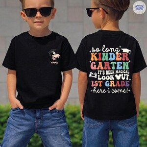 May include: Black t-shirt with a cartoon Goofy graphic wearing a graduation cap. The back of the shirt has colorful text that reads "so long KINDER GARTEN, IT'S BEEN MAGICAL, LOOK OUT 1ST GRADE +here i come!+"