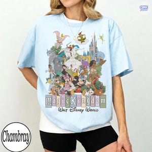 Puede incluir: Camiseta azul claro con un gr&aacute;fico colorido de personajes de Disney, incluyendo Mickey Mouse, Dumbo y Peter Pan. El texto "Magic Kingdom Walt Disney World" se muestra debajo. La camiseta tiene mangas cortas y cuello redondo.