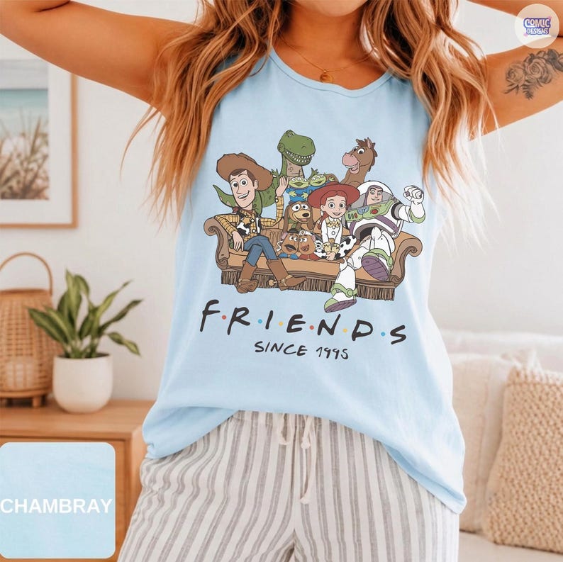 May include: A light blue sleeveless tank top featuring a graphic print of Toy Story characters sitting on a couch with the text "FRIENDS SINCE 1995" printed below. The characters include Woody, Buzz Lightyear, Jessie, Rex, Slinky Dog, and Bullseye.