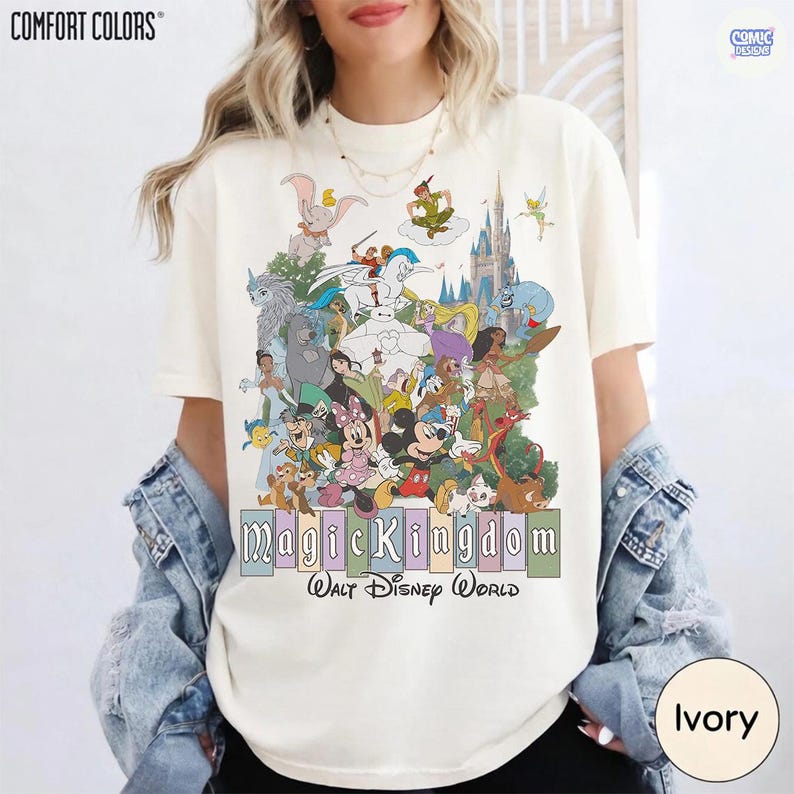 Puede incluir: Camiseta de color marfil con un gr&aacute;fico colorido de varios personajes de Disney, incluyendo Mickey Mouse y Peter Pan. El texto "Magic Kingdom Walt Disney World" est&aacute; impreso debajo. La camiseta es de la marca Comfort Colors.
