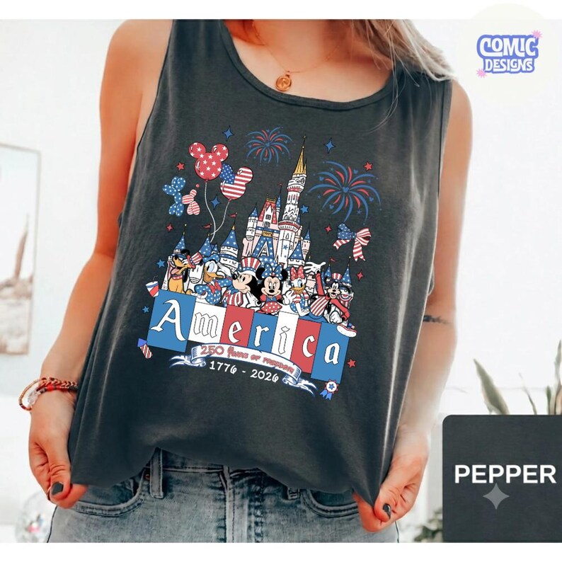 May include: A charcoal grey sleeveless tank top featuring a graphic print of a castle, fireworks, and cartoon characters wearing patriotic hats. The text reads America, 250 Years of Freedom, and 1776-2026 in red, white, and blue colours.