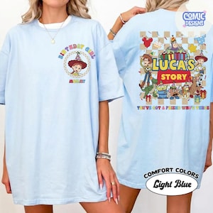May include: Pale blue t-shirt with a cartoon graphic and the words "BIRTHDAY GIRL" on the front. The back of the shirt shows "LUCAS'S STORY" with cartoon characters and the phrase "YOU'VE GOT A FRIEND WHO'S THREE."