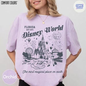 K&ouml;nnte beinhalten: Orchideenfarbenes T-Shirt mit einer Grafik von Cinderella's Schloss, Mickey Mouse und den Worten "Disney World" und "The most magical place on earth." Das Shirt zeigt auch den Text "Florida EST.1971."