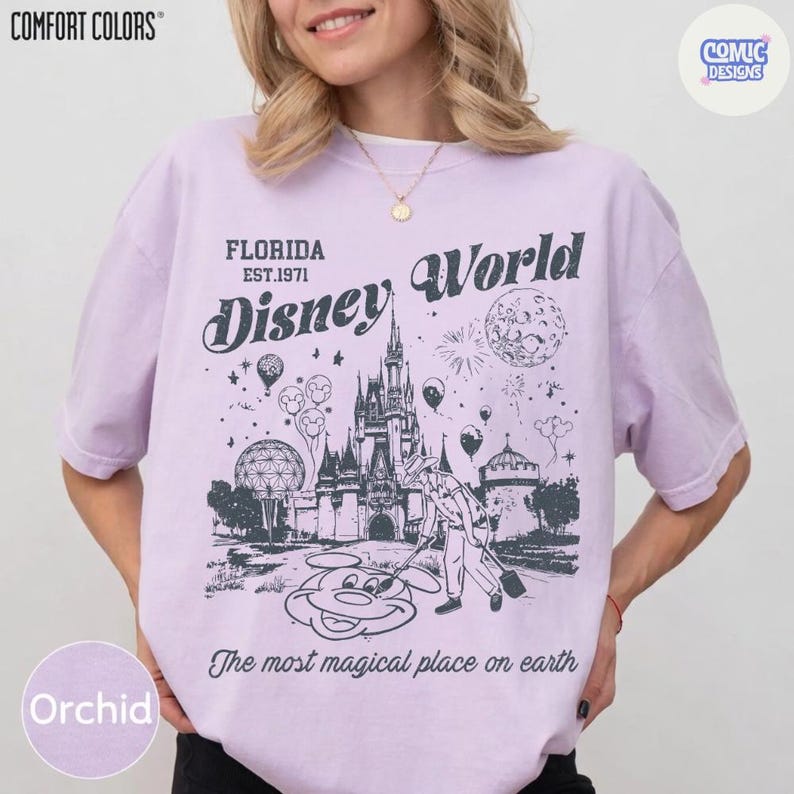 K&ouml;nnte beinhalten: Orchideenfarbenes T-Shirt mit einer Grafik von Cinderella's Schloss, Mickey Mouse und den Worten "Disney World" und "The most magical place on earth." Das Shirt zeigt auch den Text "Florida EST.1971."