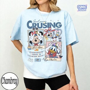 以下が含まれることがあります： ディズニーのミニーマウスとデイジーダックが描かれた水色のTシャツ。「Girl goes Cruising」の文字とその他のグラフィックが特徴です。柔らかい素材で作られており、ディズニーファンに最適です。
