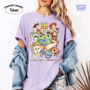 May include: A light purple t-shirt featuring a Toy Story 5 graphic with characters Woody, Buzz Lightyear, Jessie, Bullseye, and others around a cardboard box labeled Jason. The text reads Toy Story 5 and You've Got A Friend In Me.