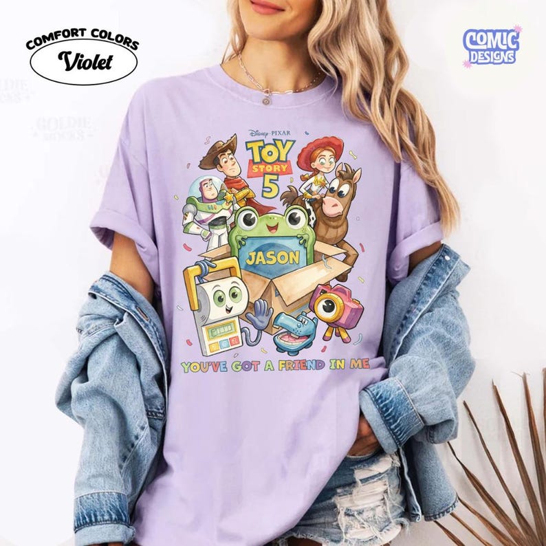 May include: A light purple t-shirt featuring a Toy Story 5 graphic with characters Woody, Buzz Lightyear, Jessie, Bullseye, and others around a cardboard box labeled Jason. The text reads Toy Story 5 and You've Got A Friend In Me.